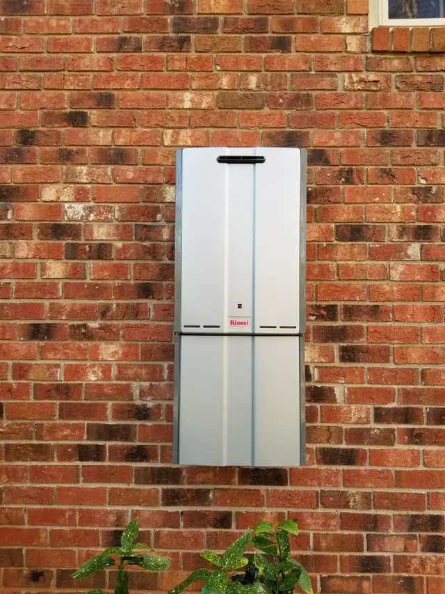 Wall-mounted tankless water heater with its gas and water piping on brick